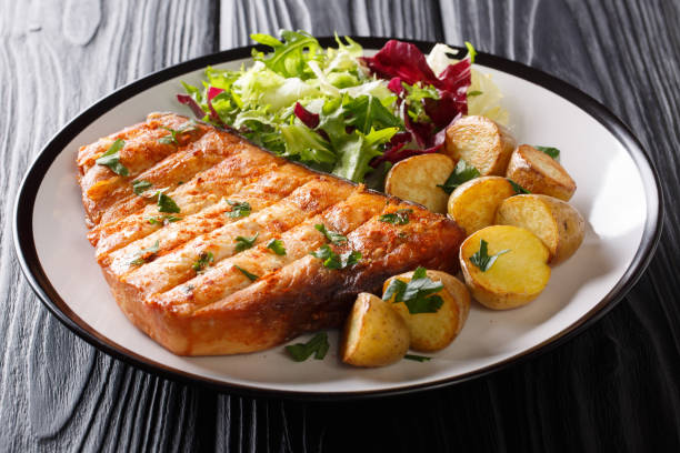 グリルステーキメカジキは、黒の背景にベビーポテトとフレッシュサラダのクローズアップを提供しました。水平 - prepared fish fish grilled close up ストックフォトと画像