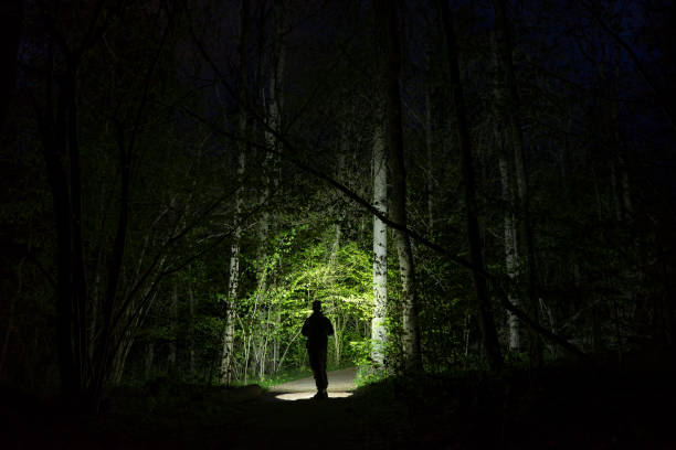 istock Man standing outdoor at dark night shining with flashlight 1147837404
