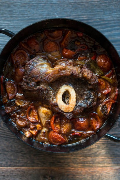 Cooked Osso Buco Veal Shanks with Vegetables in Cast-Iron Pot on Wooden Background Cooked Osso Buco Veal Shanks with Vegetables in Cast-Iron Pot on Wooden Background ossobuco stock pictures, royalty-free photos & images