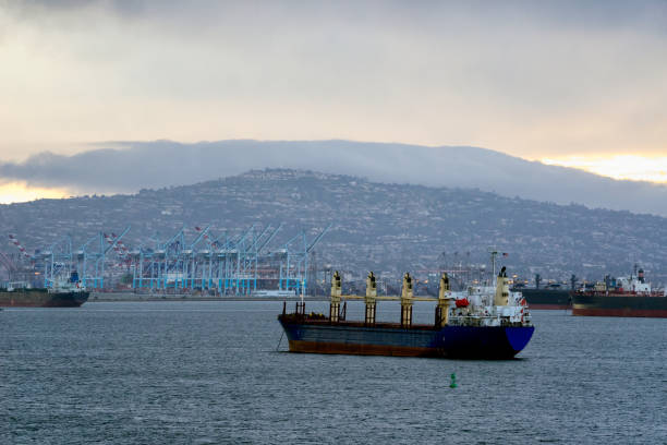 город энсенада, мексика на заднем плане с баржей, проходящей мимо в коммерческой судоходной гавани - barge beach large blue стоковые фото и изображения