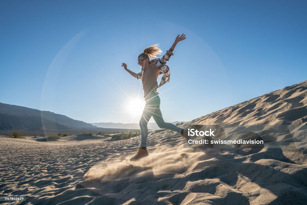Best vacations ever !! Young woman running down sand dunes at sunset enjoying vacations and being playful Running Stock Photo