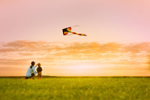 Mother and son having fun flying a kite at sunset