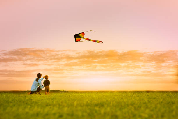 mor och son ha kul flygande en drake vid solnedgången - flying kite bildbanksfoton och bilder