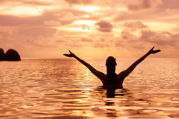 Woman in the water with her arms outstretched enjoying the beautiful sunset.  Location Koh Tao, Thailand.