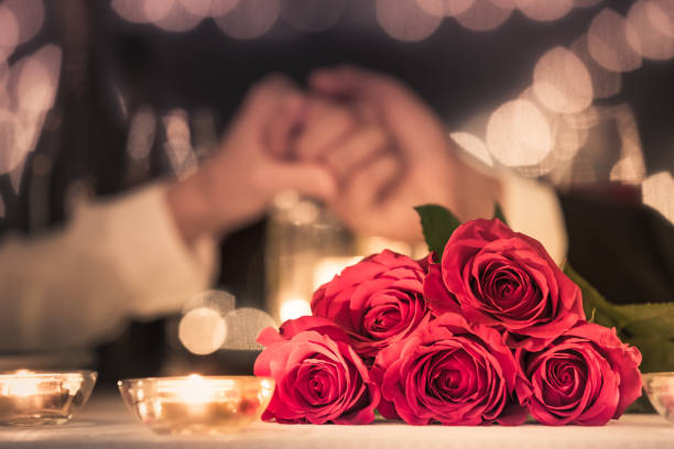 Romantic dinner Couple at a candle light dinner date holding hands next to bouquet of red roses. valentines day stock pictures, royalty-free photos & images