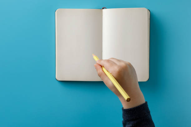 istock Child hands holding a large spiral notepad with mockup for your design. Blue background. 1147852419