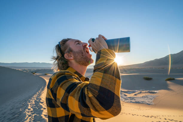 jeune homme dans le désert restant sur des dunes de sable buvant de la bouteille d'eau - thirsty desert men reaching photos et images de collection