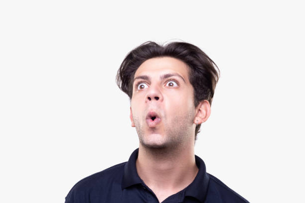 Low angle portrait of shocked young man looking away over white background Low angle portrait of shocked young man looking away over white background. Horizontal composition. Studio shot. confusion raised eyebrows human face men stock pictures, royalty-free photos & images