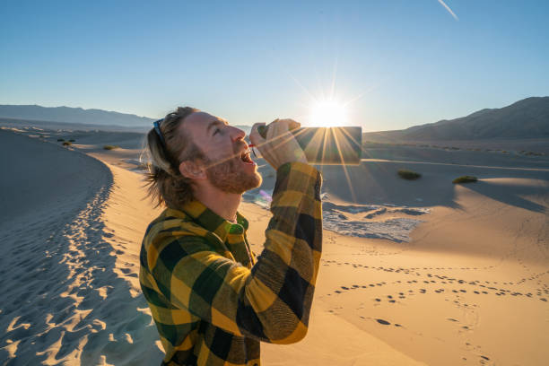 물 병에서 마시는 모래 언덕에 서 있는 사막에서 젊은 남자 - thirsty desert men reaching 뉴스 사진 이미지