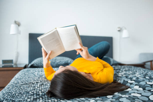 istock Young brunette woman reading a book and lying down on the bed 1147875843