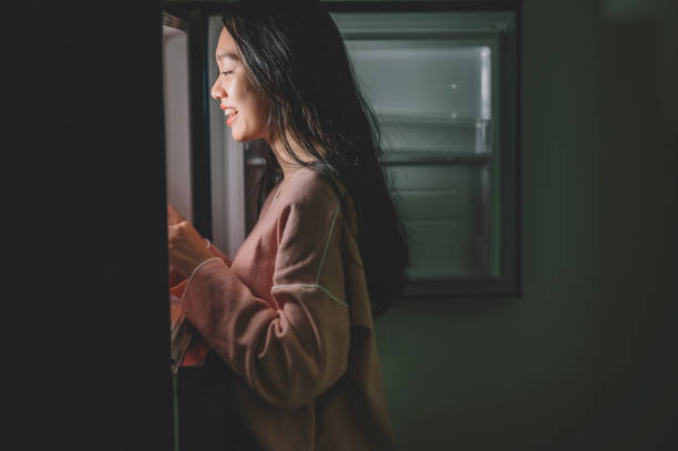 ein asiatisches chinesisches weibchen, das in der nacht in der küche nach nahrung aus dem kühlschrank sucht und einen teller hält - raum eine person dunkelheit stehen gegenlicht stock-fotos und bilder