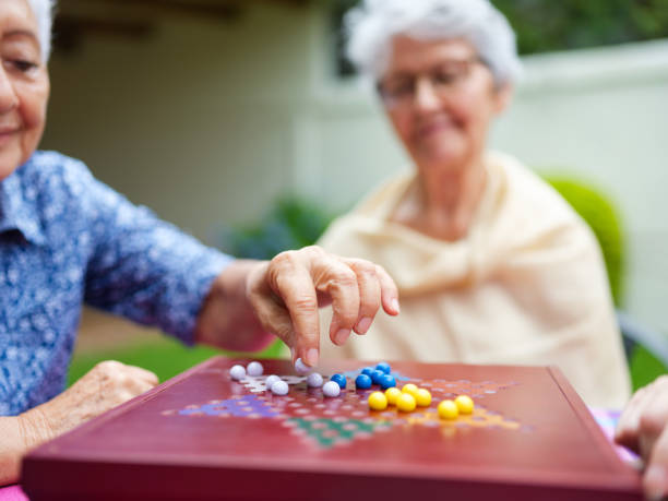 Image focused on elderly women playiing chinese checkers Image focused on the hand of an elderly woman making move on the board game chinese checkers and smiling. chinese checkers stock pictures, royalty-free photos & images