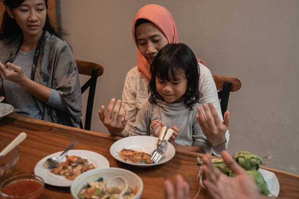 istock mom and daughter pray before eating 1147894682