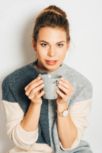 istock Beautiful woman holding cup of coffee or tea, wearing grey pullover, posing against white background, studio shot 1147898794