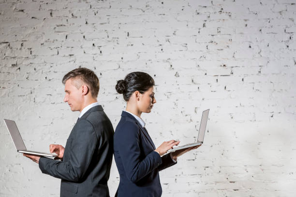 Side view of business colleagues using laptops by white brick wall at office