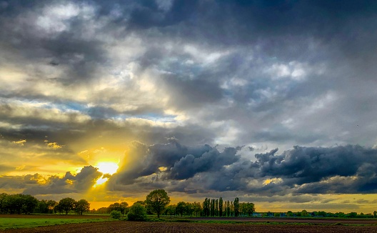 Golden sun breaking through the dark grey threatening storm clouds over a Countryside pasture landscape