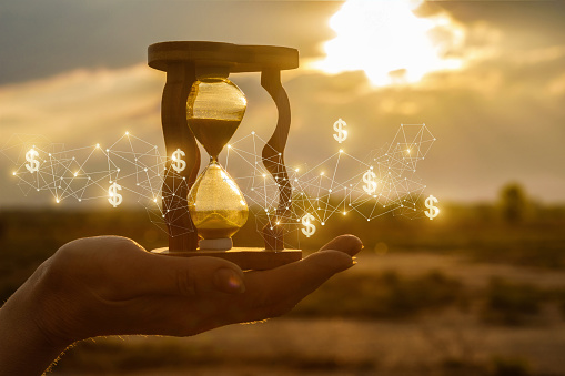 The concept of time and the new financial ideas. Hourglass in hand with and financial structure at sunset.