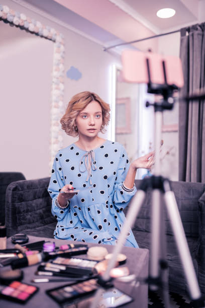 istock Appealing blogger sitting at table with cosmetics filming video 1147912317