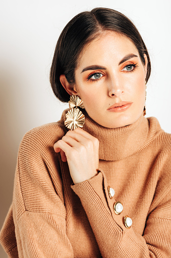 Studio shot of beautiful young woman with dark hair and blue eyes, , wearing brown makeup and turtle neck pullover