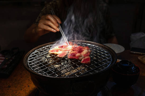 Female hand with chopsticks holding raw beef on charcoal grill stock photo