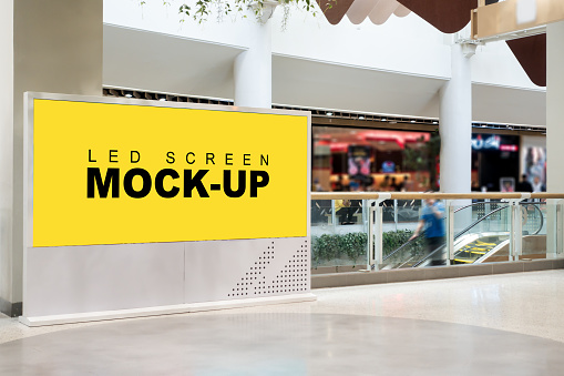 Mock up large LED blank yellow screen billboard on modern frame near escalator with clipping path in mall, blurred man standing on escalator scroll down, empty space for advertising or information
