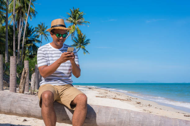 istock Young asian man on the beach using smartphone. 1147924065