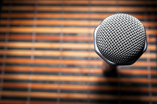 Top-Down View of A Microphone Head and Silver Grille on A Striped Yellow and Black Bamboo Mat Background. Karaoke Bar, Party Concept. Copy Space.