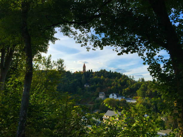 View of Clervaux and the mountain and forest between two trees.