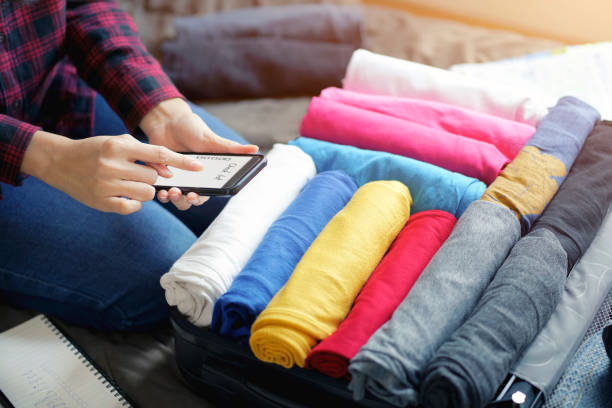 istock Woman hands using smartphone write checklist to prepare accessories for new journey, packing clothes in suitcase bag on bed. 1147931407