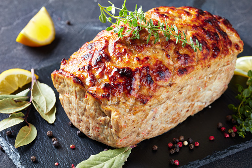delicious whole chicken meatloaf served on a slate tray with lemon slices and fresh thyme on a concrete table, horizontal view from above, close-up