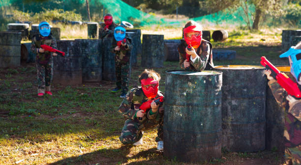 Children paintball players of opposite teams playing in shootout outdoors Glad cheerful positive smiling children paintball players of opposite teams playing in shootout outdoors paintball photography stock pictures, royalty-free photos & images