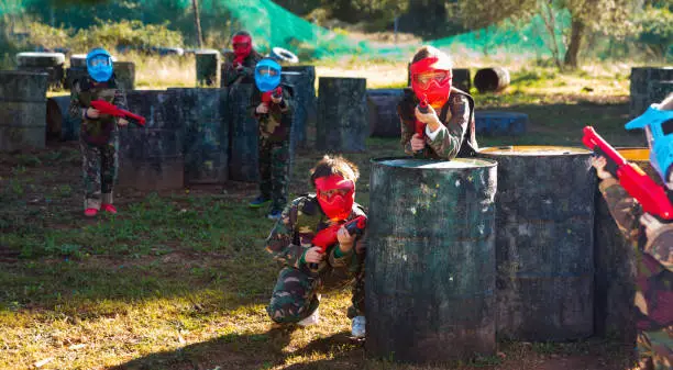 Photo of Children paintball players of opposite teams playing in shootout outdoors