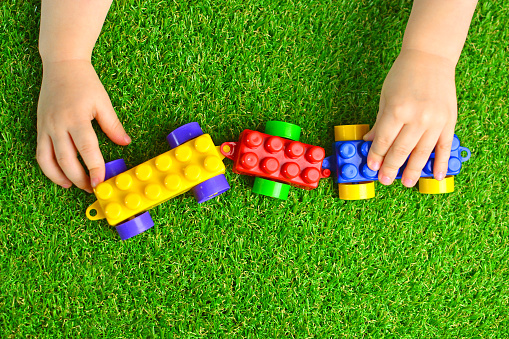Artificial turf. Baby plays with a building kit train on a green artificial grass. Kindergarten background.
