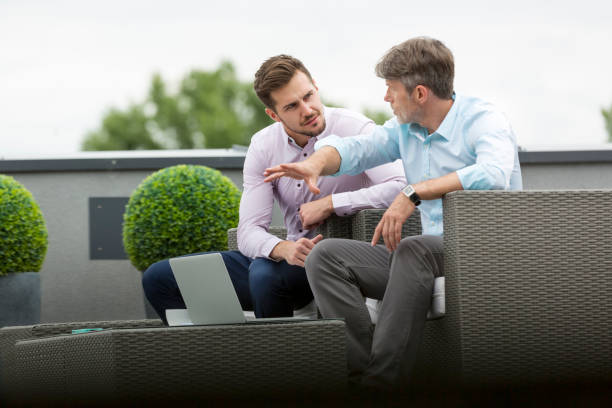 istock Businessmen discussing over laptop while sitting at office terrace 1147936369