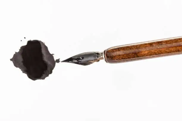 top view of black painted nib of brown penholder and black ink blot on white paper