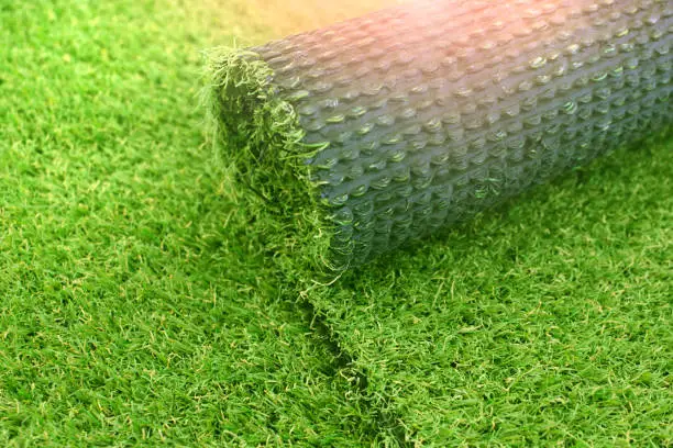 Artificial turf laying background. Roll of an synthenic grass layer. Greenering of the yard with an artificial lawn.