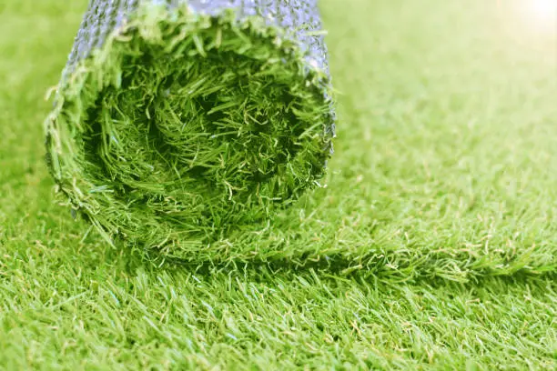 Artificial turf roll. Synthetic grass lawn laying background.