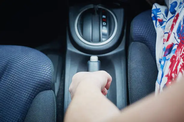 A high-angle look at a female hand pulling up the emergency or parking brake of her car.