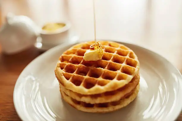 Shot of a stack of waffles topped with a cube of butter and syrup on a plate