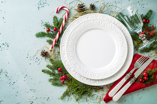 Elegant christmas table setting design captured from above (top view, flat lay). Empty white plate, glass, cutlery, candy cane and decorations. Background layout with free text (copy) space.