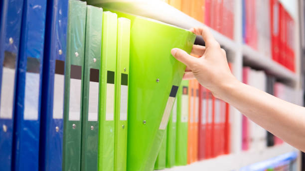 istock Male hand choosing new green ring binder file folder from colourful shelf display in stationery shop. Buying office supplies concept 1147969684