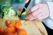 Woman's hand slicing broccoli on wooden chopping board