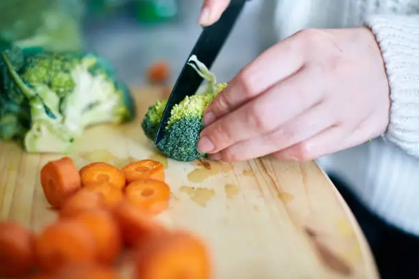 Photo of Woman's hand slicing broccoli on wooden chopping board