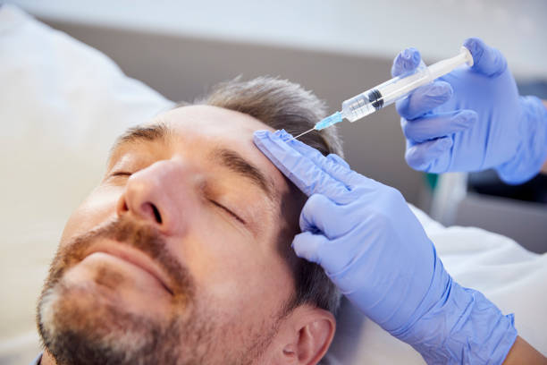 female beautician giving mature male patient botox injection in forehead - lifting device imagens e fotografias de stock