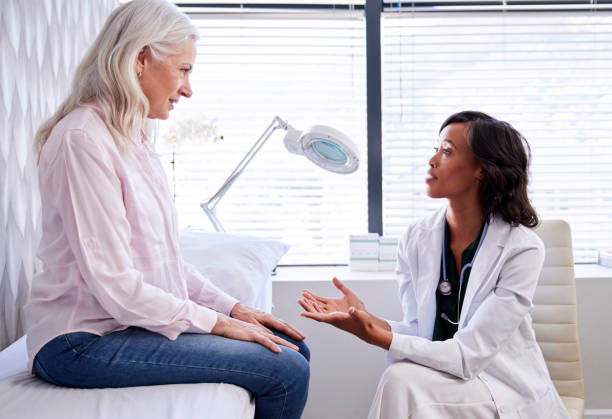 mature woman in consultation with female doctor sitting on examination couch in office - patient doctor african descent hospital imagens e fotografias de stock