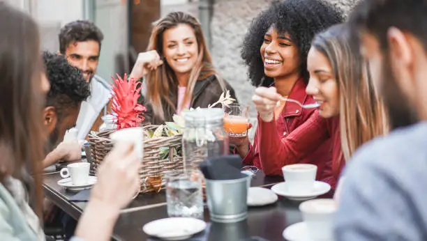 Group of happy friends drinking coffee and cappuccino at vintage bar outdoor - Young millennials people doing breakfast together - Friendship, youth and food concept - Focus on afro girl face