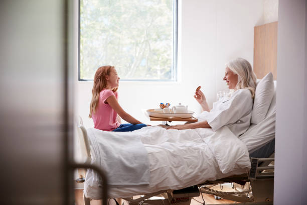 アフタヌーンティーのための病院のベッドで祖母を訪問する孫娘 - happiness women senior adult two people ストックフォトと画像