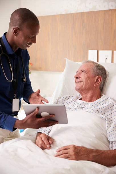 doctor with digital tablet visiting and talking with senior male patient in hospital bed - male nurse black nurse doctor imagens e fotografias de stock