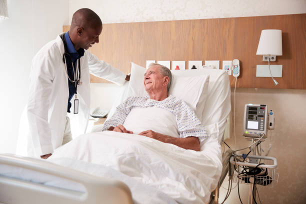 doctor visiting and talking with senior male patient in hospital bed - male nurse black nurse doctor imagens e fotografias de stock