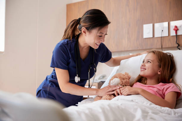 female nurse visiting girl lying in hospital bed hugging teddy bear - hospital patient bed nurse imagens e fotografias de stock